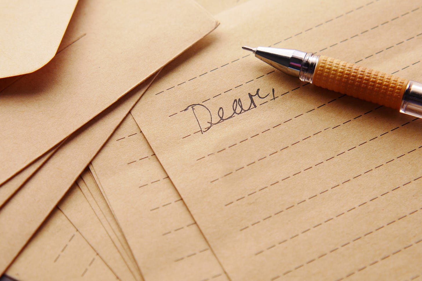 Sheets of lined notepaper with a mechanical pencil; one sheet reads "Dear" in handwriting.