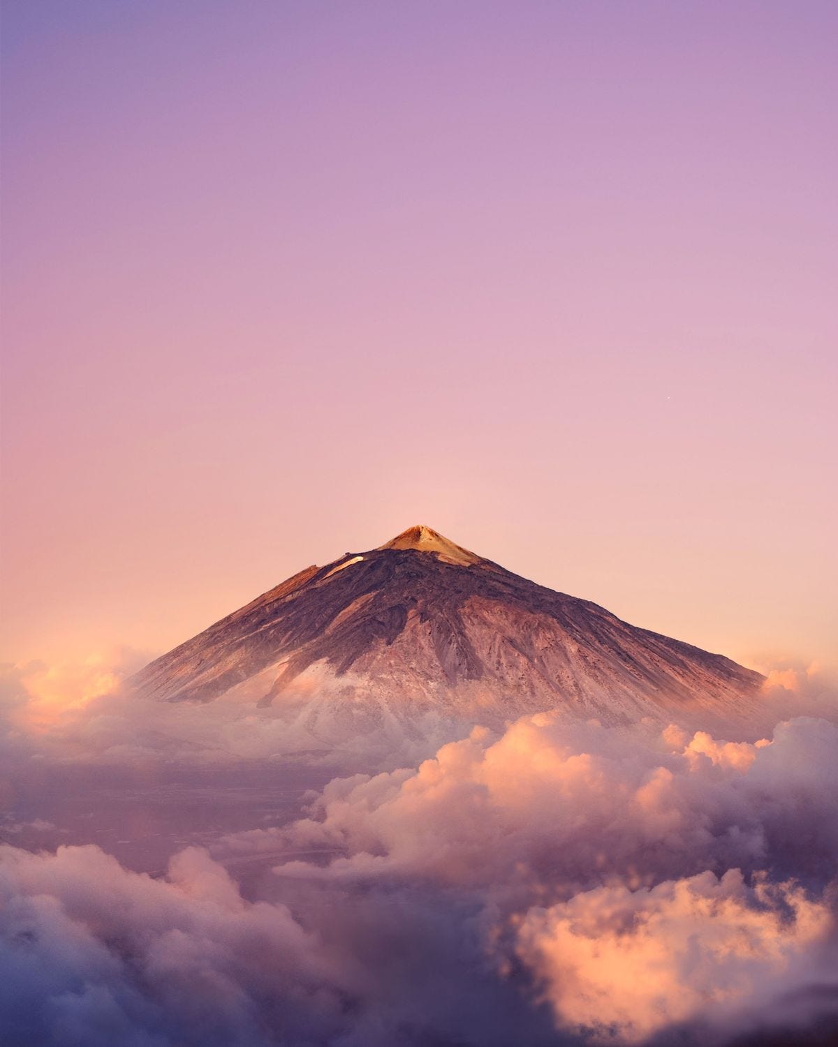 pico de um vulcão aparecendo acima de uma camada de nuvens brancas