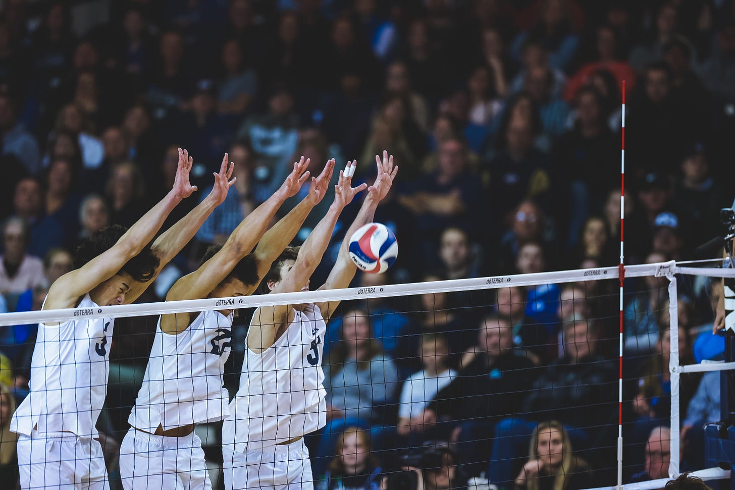 Three volleyball players jumping at the net with hands in the air