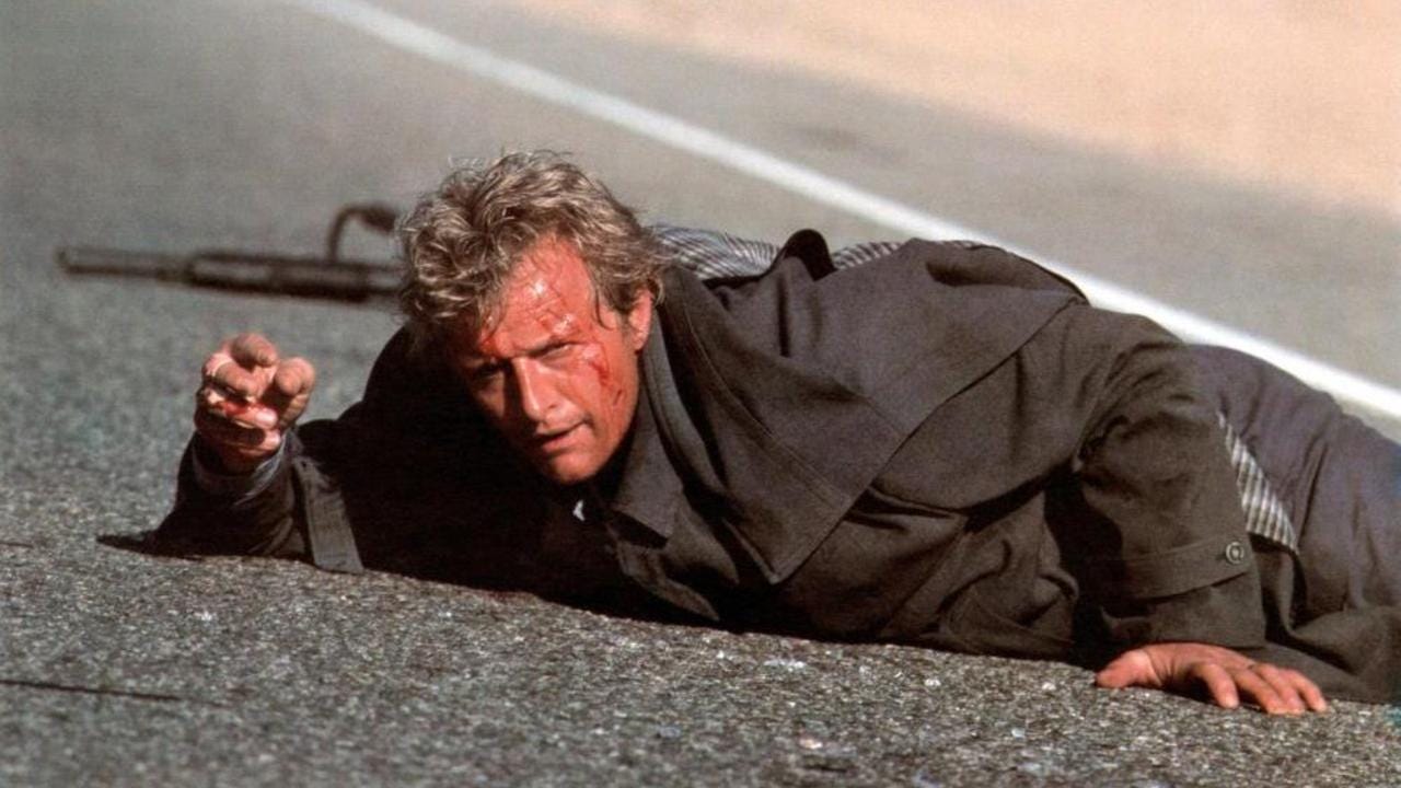 Movie still from The Hitcher. A man lies on the pavement, bloodied and with a gun behind him