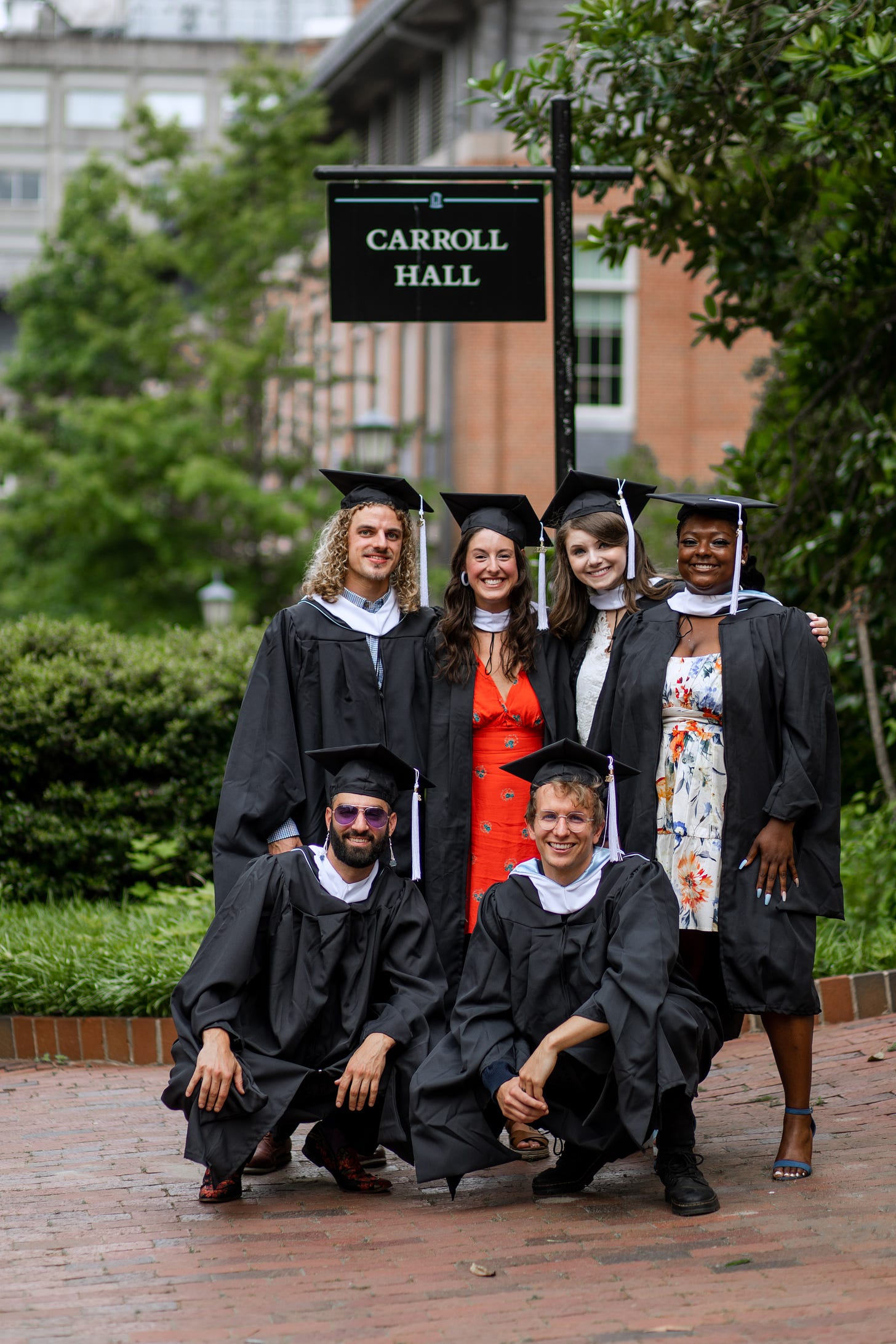 My cohort stands in front of the sign for Carroll Hall wearing our graduation robes.