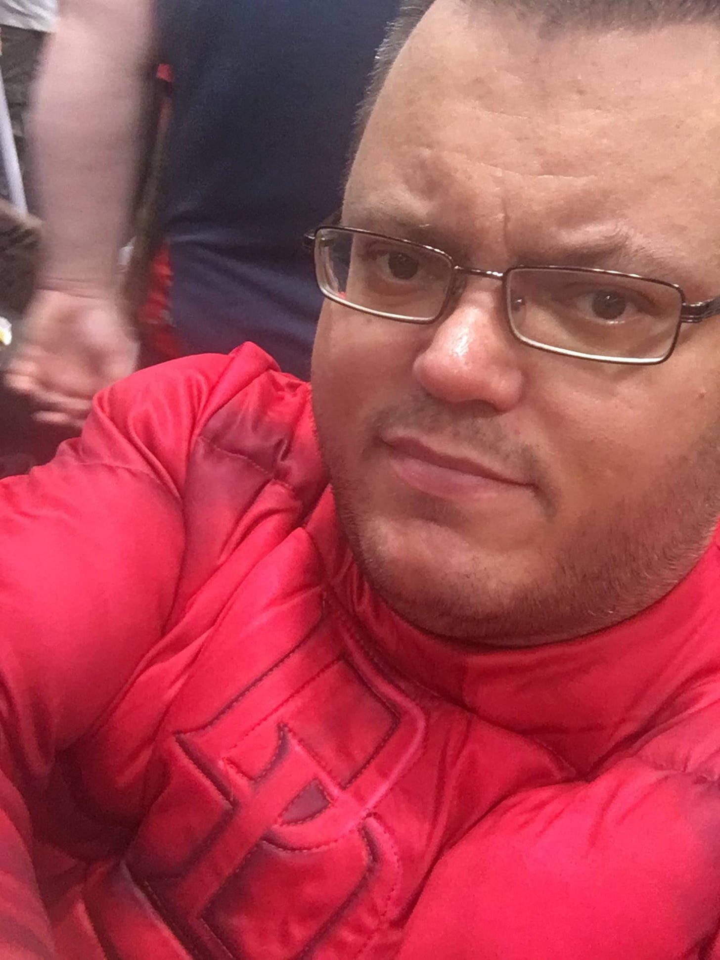 Close-up photo of a bespectacled man (Sam) with a wistful smile, wearing a red superhero costume.