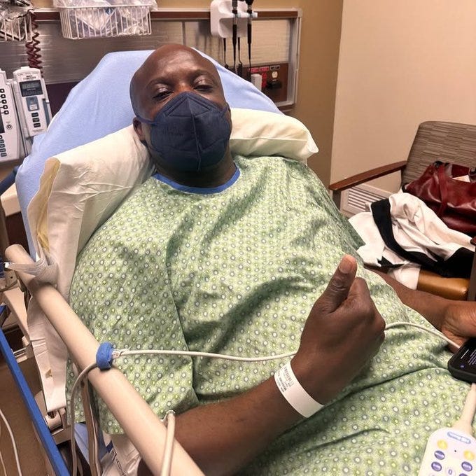 Mayor Yemi in a hospital bed giving a thumbs up