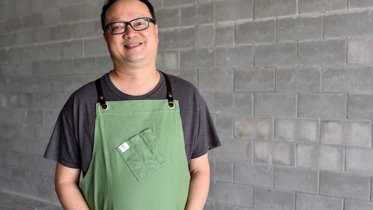 An image of chef Au-Yeung, who is standing with his hands in his apron pockets. The apron is green.
