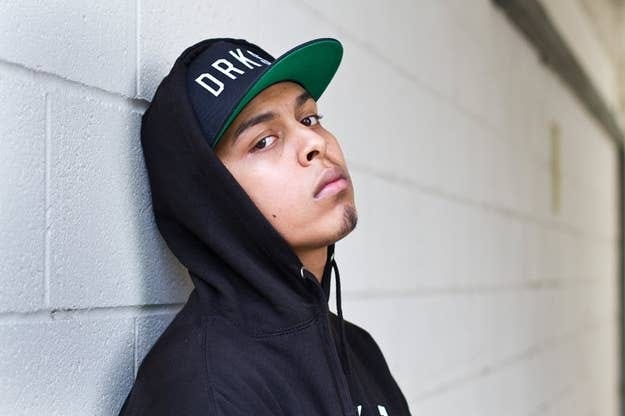 Person in a cap and hoodie, looking thoughtfully towards the camera