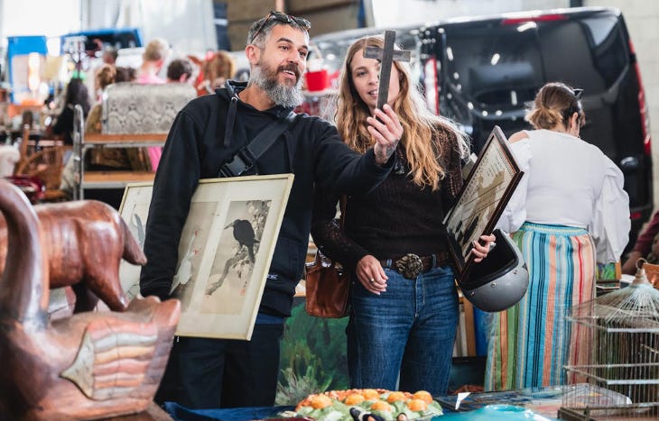 A man and woman examining a wooden cross at a flea market