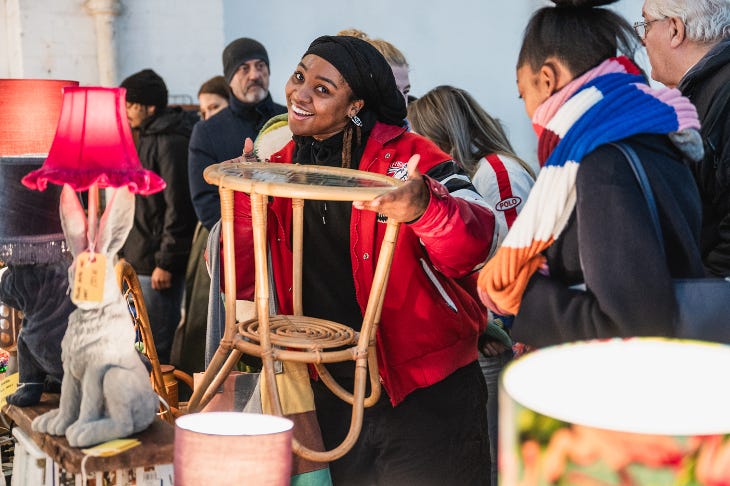 A woman posing with a coffee table and smiling at a flea market