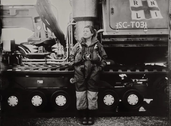 Black and white photo of a woman standing in front of an RNLI lifeboat