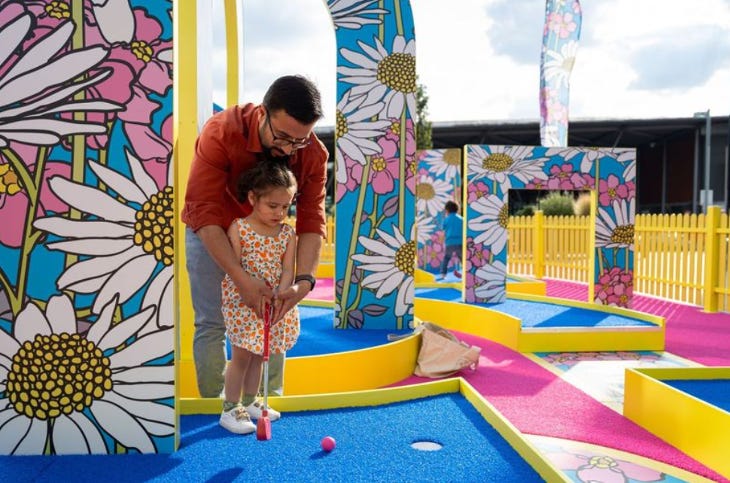 A man and young girl playing crazy golf against a colourful backdrop