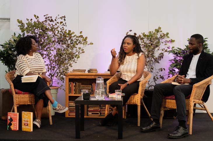 Three people sitting in chairs on stage talking, in front of a bookshelf