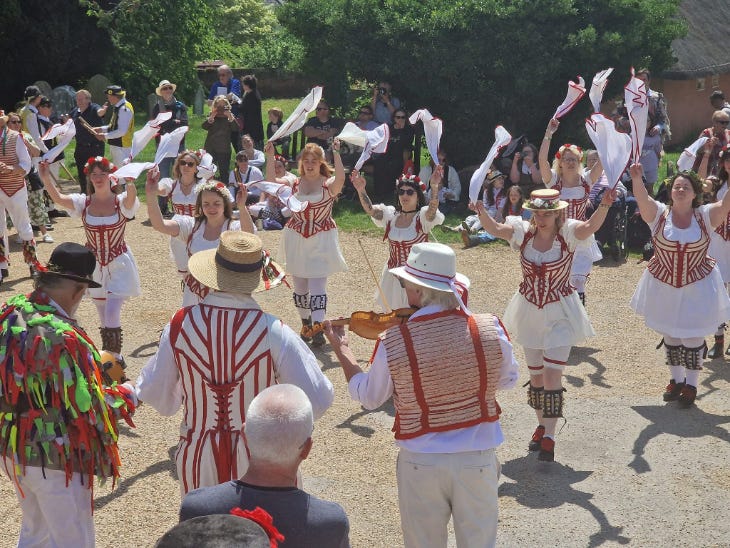 Morris dancers performing in red and white costume in the sunshine