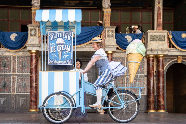 A woman riding an old-fashioned ice cream bicycle on stage at the Globe