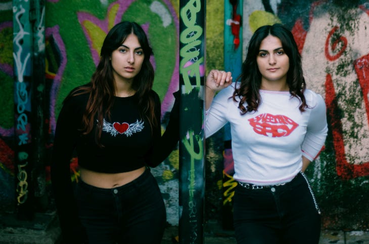 Two women standing against a grafitti wall backdrop looking at the camera