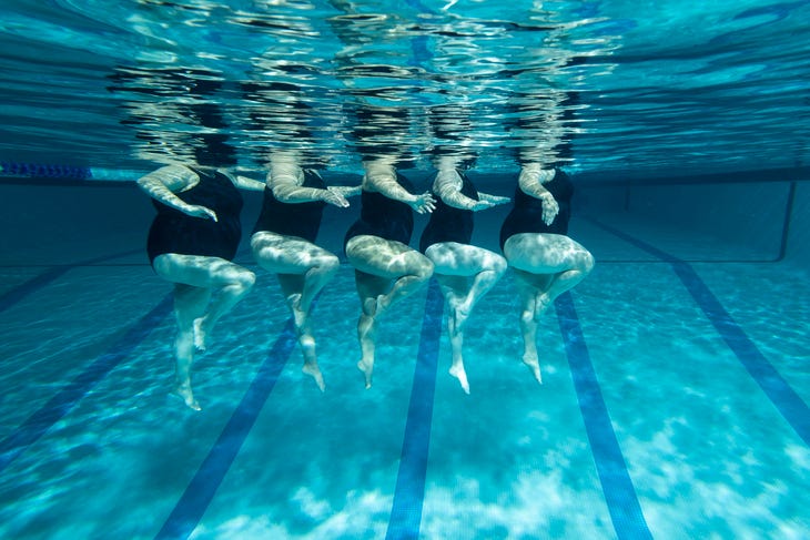 Five swimmers in a pool, only their legs and bodies are visible underwater