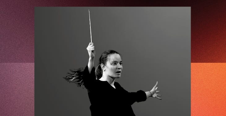 A conductor with baton raised high in her right hand, and her left hand outstretched