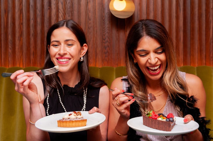 Two young women sitting side by side, each holding a plate with a slice of pie