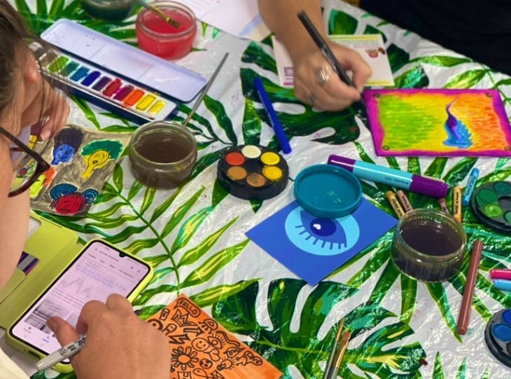 A photograph of people painting, with various paint palletes laid out on a table