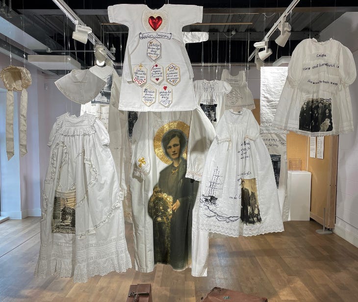 White dresses decorated with various images and messages, hanging in a gallery