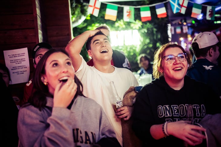 Three people watch sport in a pub. We can't see what they're watching, but they look delighted. 