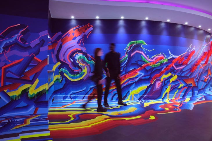 Two people walking past a colourful wall at London Art Fair