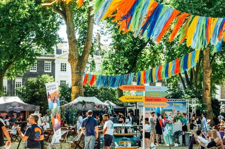 People sitting and standing around in the sunshine in a garden, beneath colourful bunting