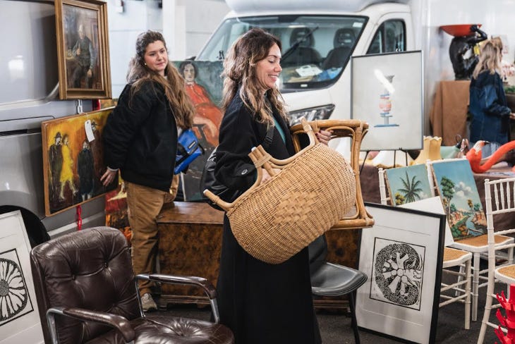 A woman carrying a wicker chair through a flea market