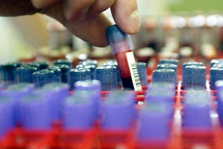 Hand removing a vial of blood for testing at a clinic.