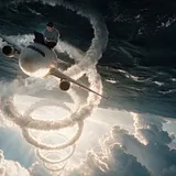 A white airliner climbs nose up through an upside-down world, a spiral vapour trail coiling behind it back toward…
