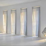 A bright empty white room with a row of tall windows, one sheer curtain caught and billowing inward on the wind.