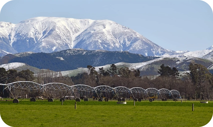 snowy mountains with big irrigators in a field in the foreground