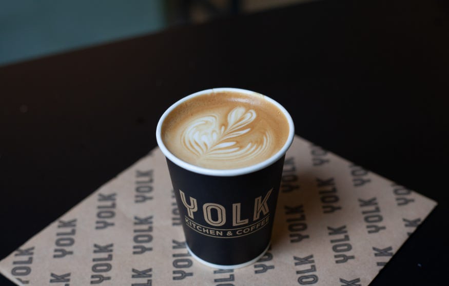 A cup of coffee in a Yolk branded takeaway cup