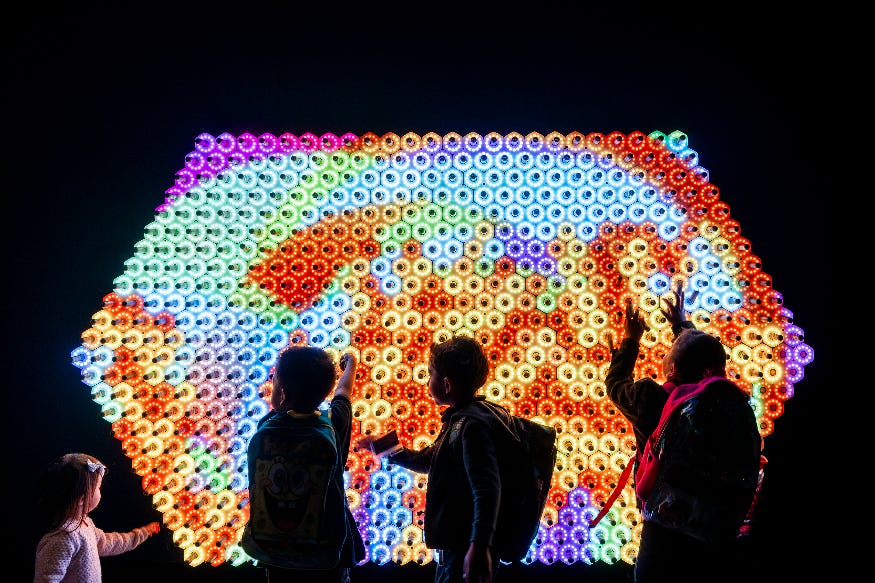 People silhouetted in front of a glowing, colourful wall