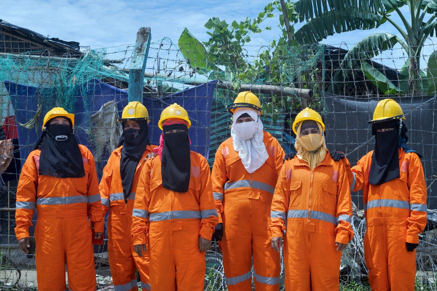 A group of women wearing face coverings, hard hats, and hi-vis orange suits