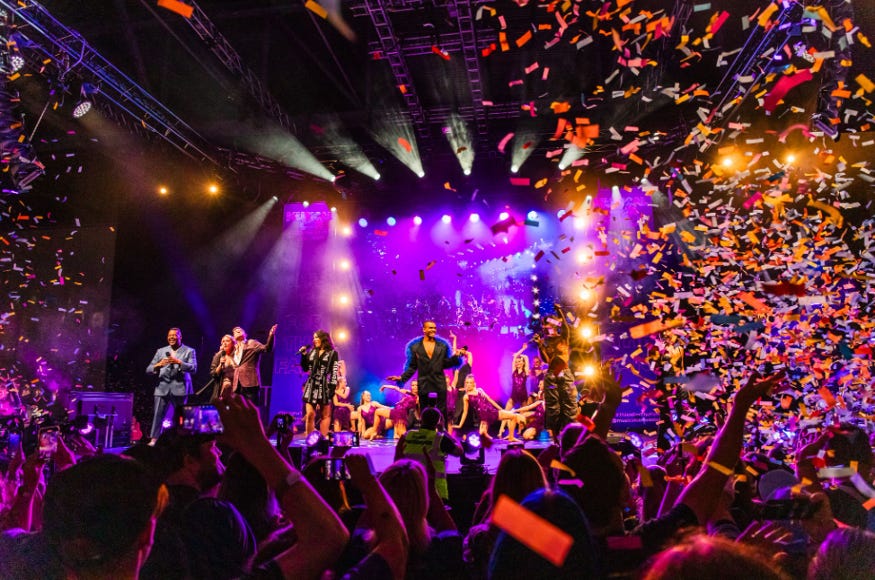 Confetti falling as a crowd watches six performers on stage at Musical Con