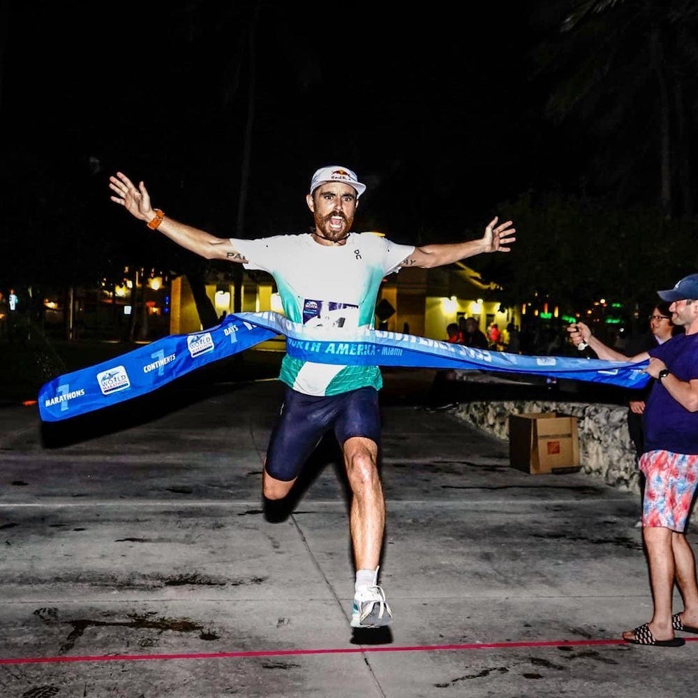 A man crosses a finish line that is blue to a crowd at night