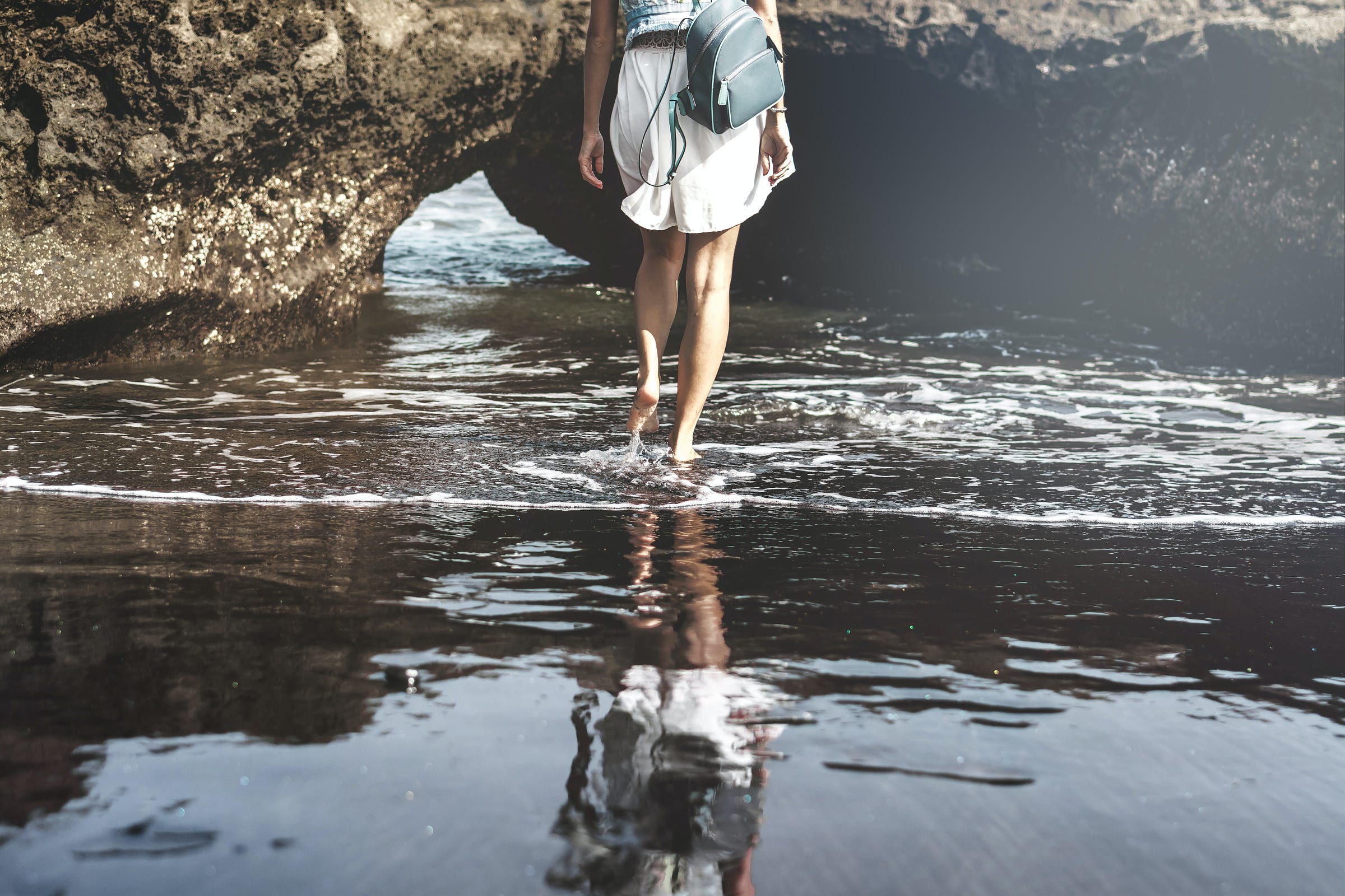 woman walking through water towards large rock with backpack