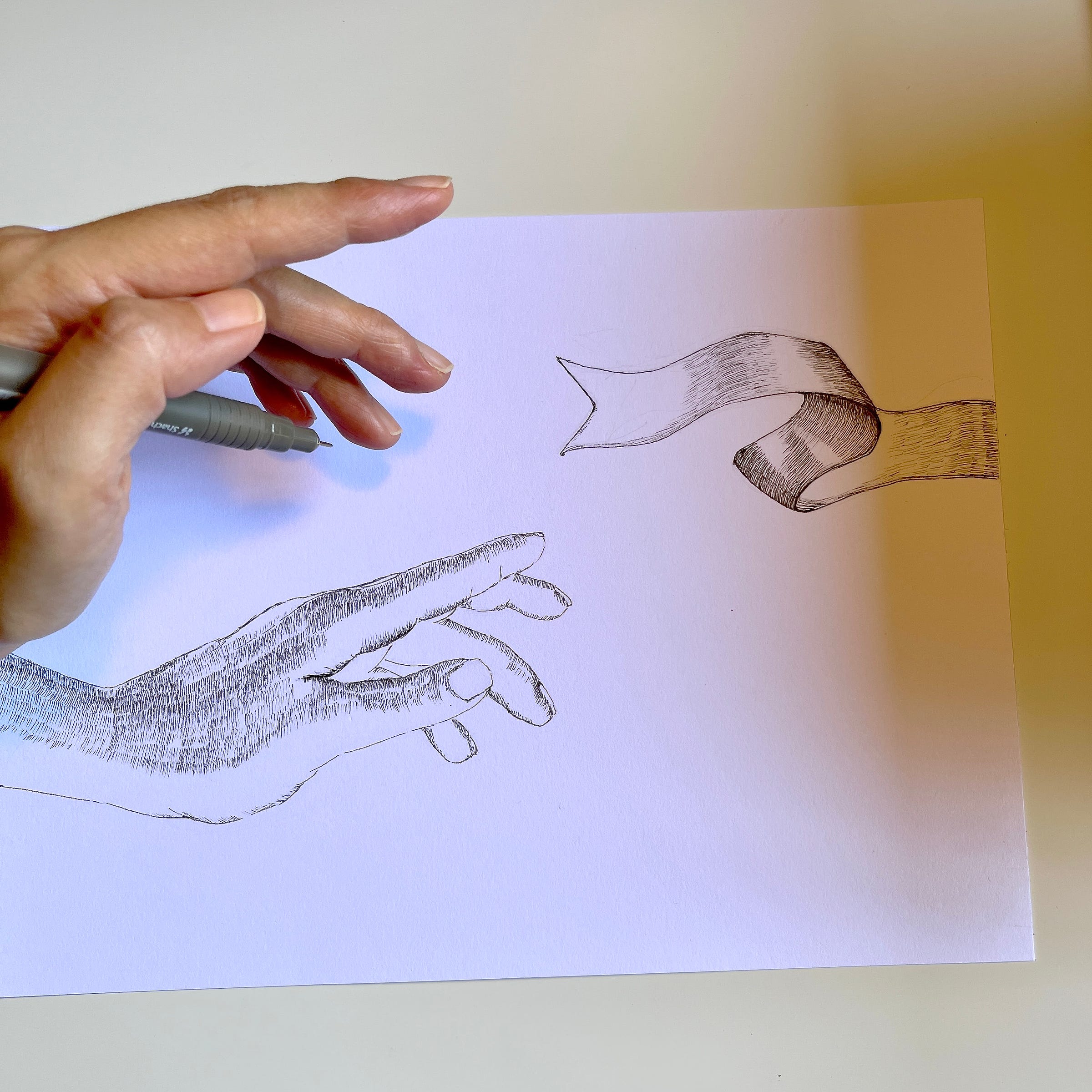 Image: photo of my hand, holding a pen on top of a black & white line drawing. The left side of the drawing shows the hand of a person letting go of something. The gesture of the fingers felt like they are hanging in mid-air, as if the person is hesitant, yet because of love, determined to let go. The right side of the drawing shows part of a ribbon softly flying away, the end of the ribbon facing towards the hand of the person, looking like it’s reaching out to the one releasing it, saying goodbye, yet thankful to be given the chance to fly.