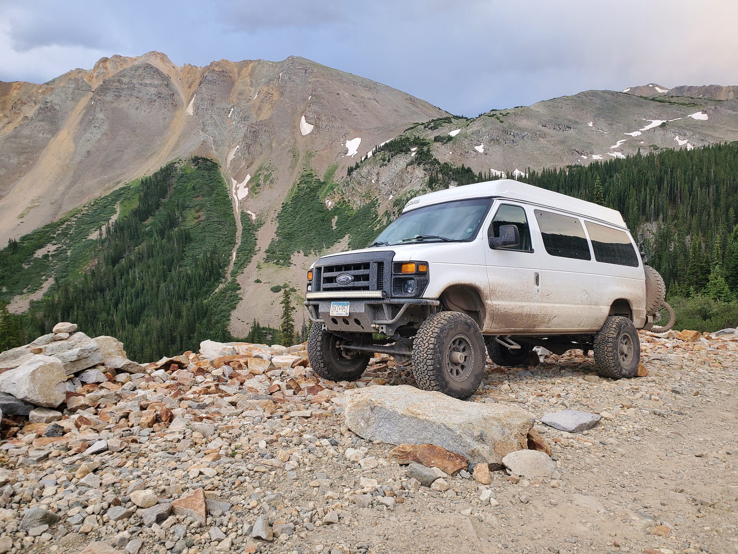 A heavily-modded van stands off-road with mountains in the background