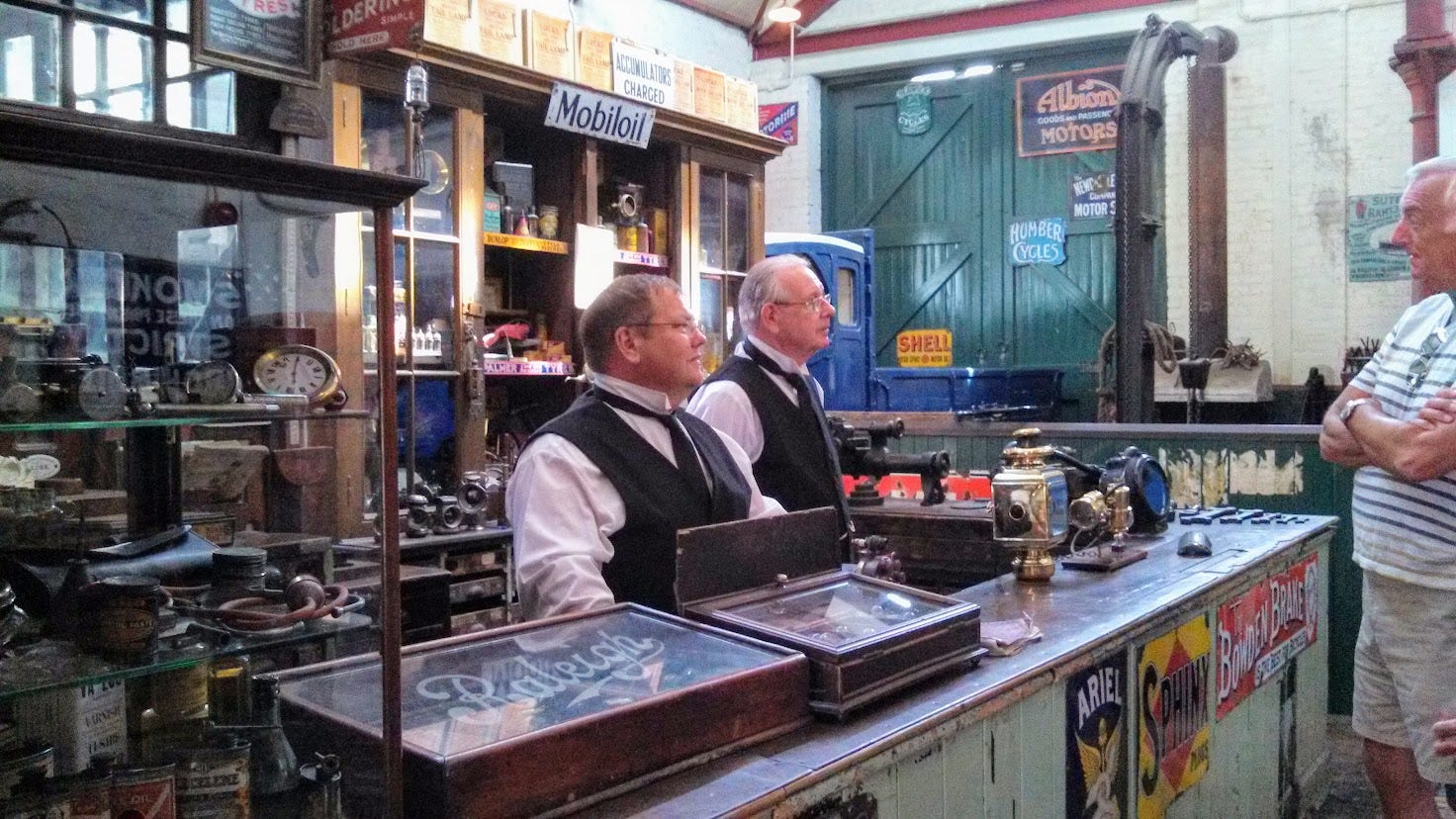 Edwardian car repair shop with staff and tourist