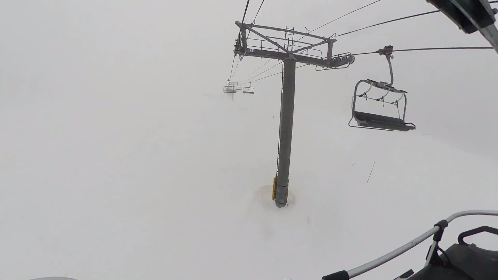 a ski lift tower and a few chairs are visible. Whiteout conditions make it hard to tell the ground apart from the sky