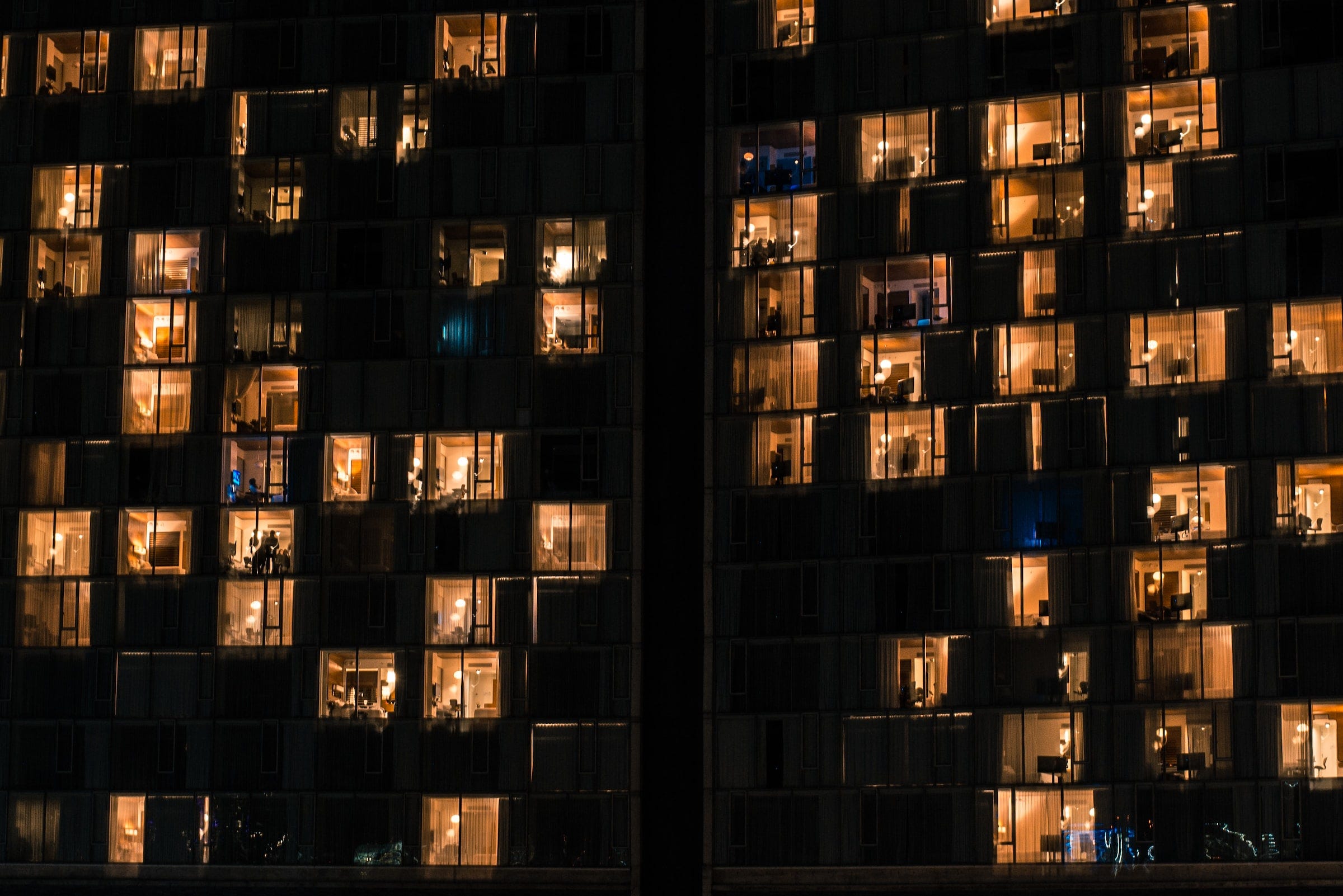 Le finestre illuminate di un grande edificio, probabilmente un grattacielo: è già notte e molte finestre del palazzo sono illuminate. Alcune di loro sono schermate da tende, altre invece lasciano trasparire la vita delle case e degli uffici.