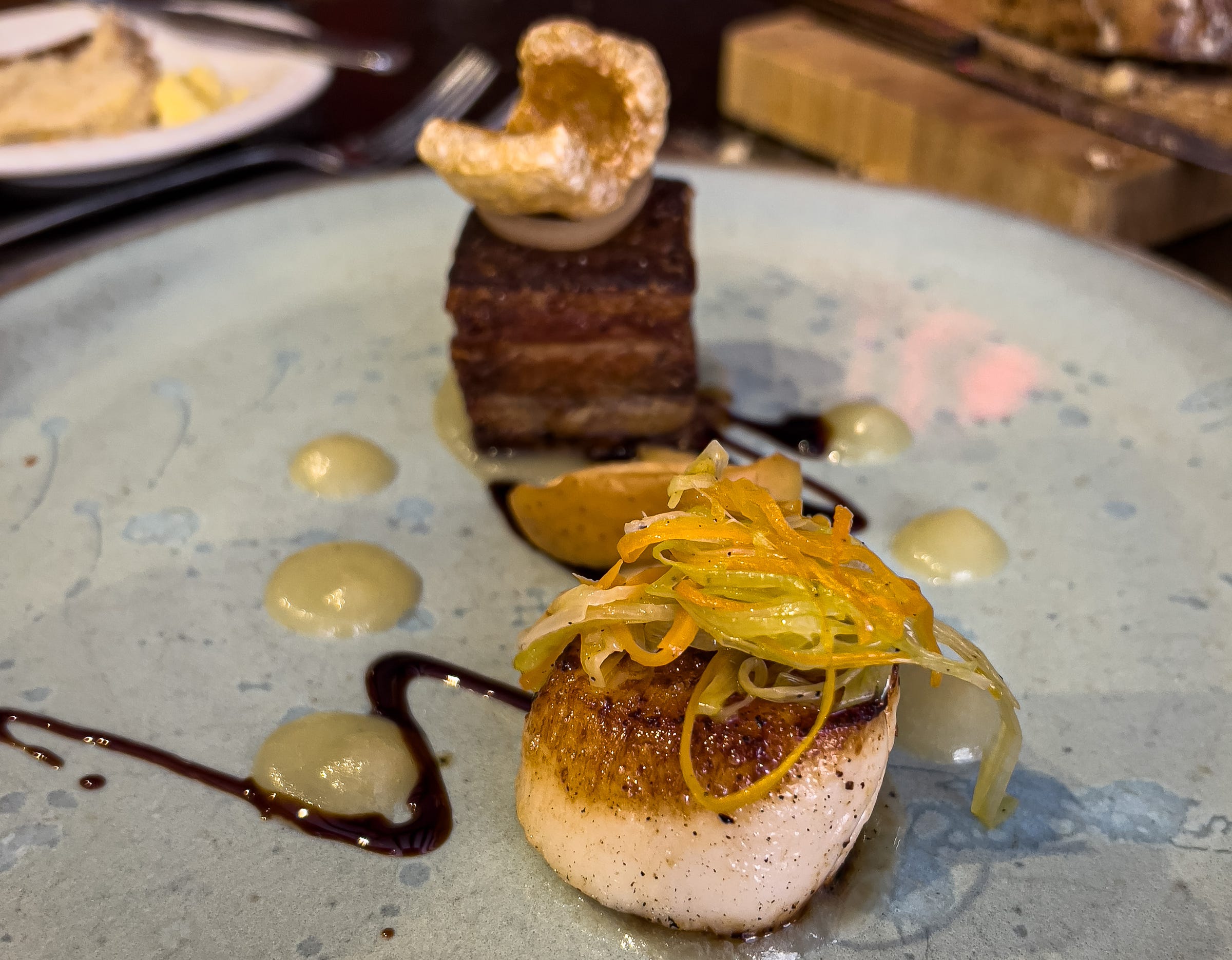 Orkney scallop, old spot belly pork, ginger veg, and poached apple on a plate at the 5 North Street Restaurant in Winchombe, England