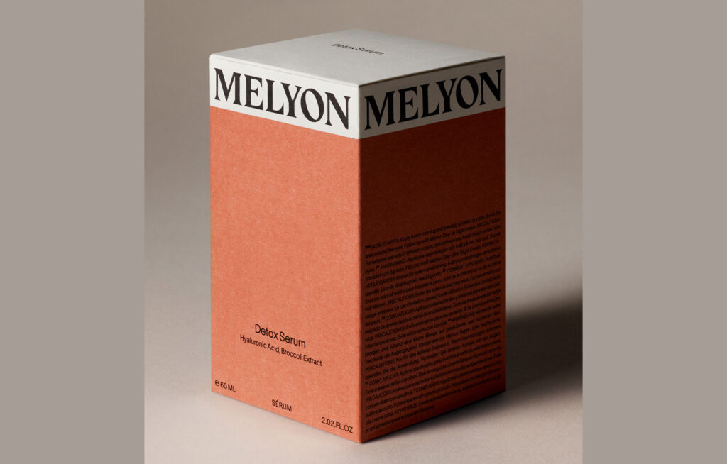 Photograph of a red Melyon Detox Serum box. It is made of paper, primarily red with a white band at the top, and one of its corners is closest to the camera.