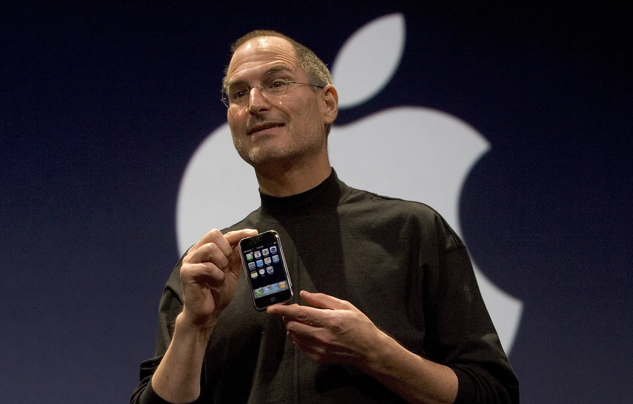 Photo of Steve Jobs seen from below, holding the original iPhone at the 2007 unveiling of the device