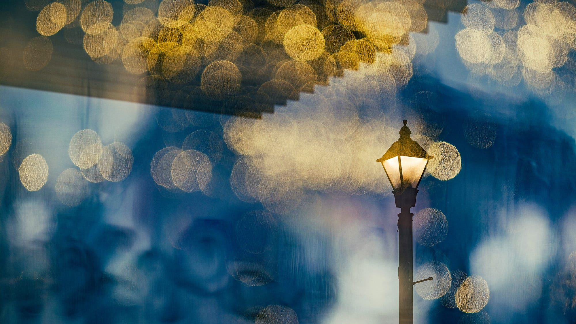 A light post near the lake is illuminated. A second photograph with bokeh is superimposed on top of the base photograph. 