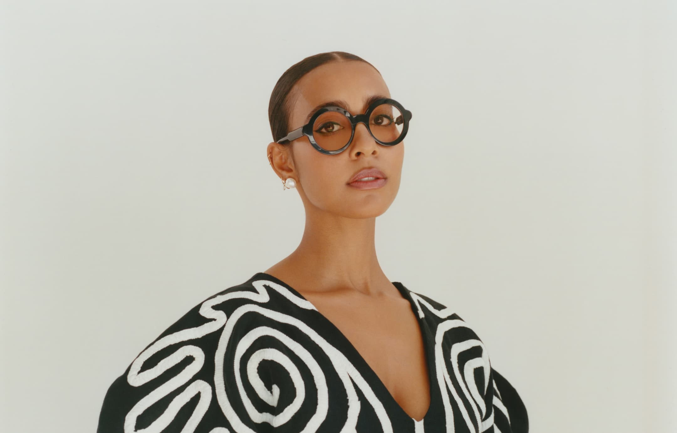 Bust-length portrait of Hannah Traore, who is wearing thick black glasses and a black-and-white swirl-print top.