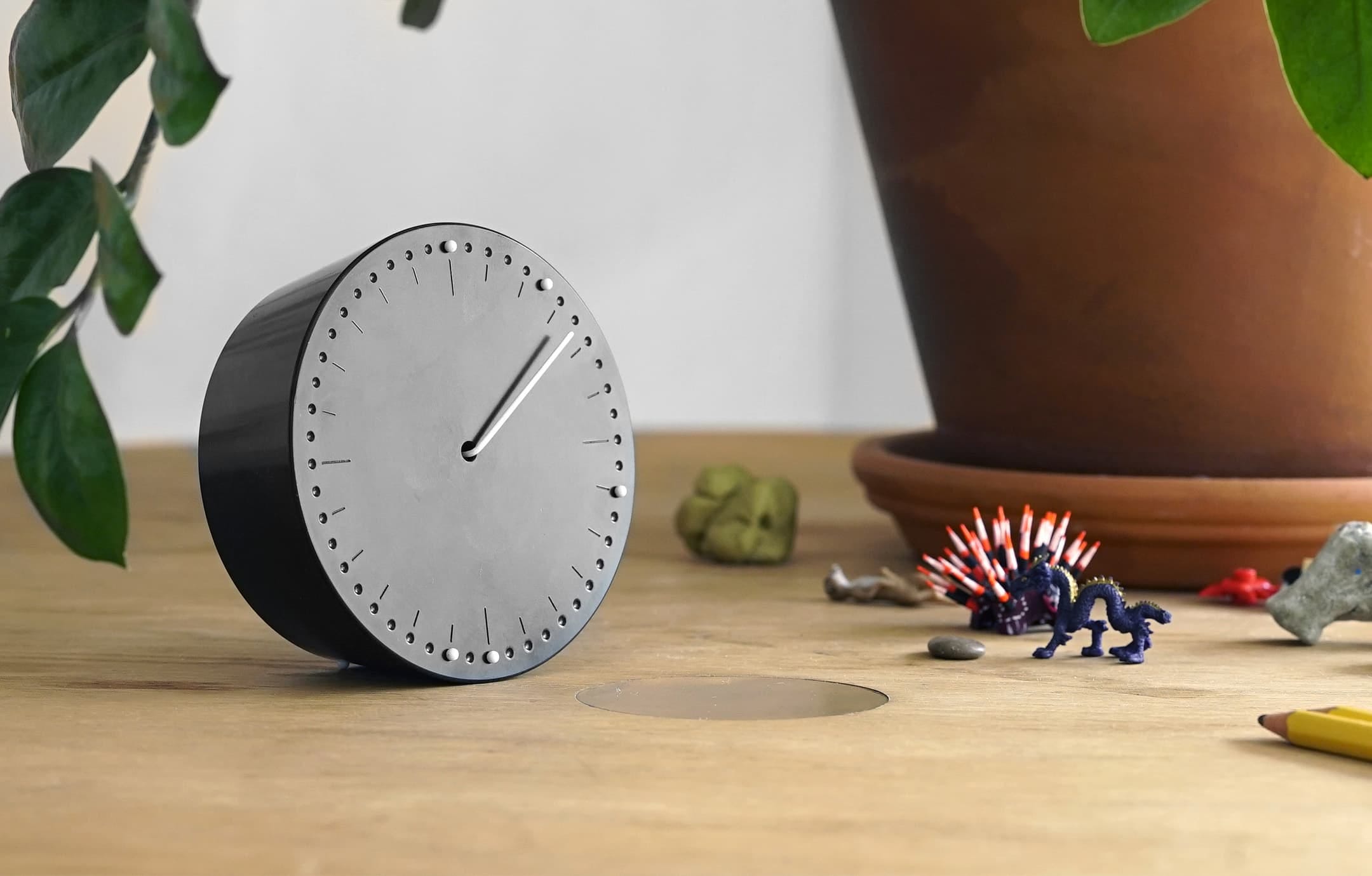 Photograph of a Superlocal clock, by CW&T, on a desk with kids’ toys and a potted plant in the background