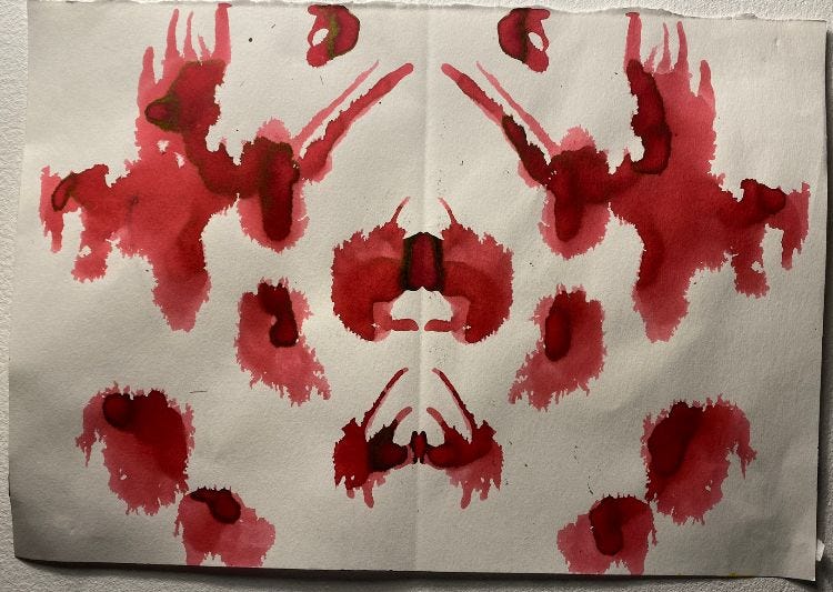A piece of paper showing a Rorschach style ink blot, printed in red. The print resembles a bear’s face and claws. Maybe. Or blood. Something like that.