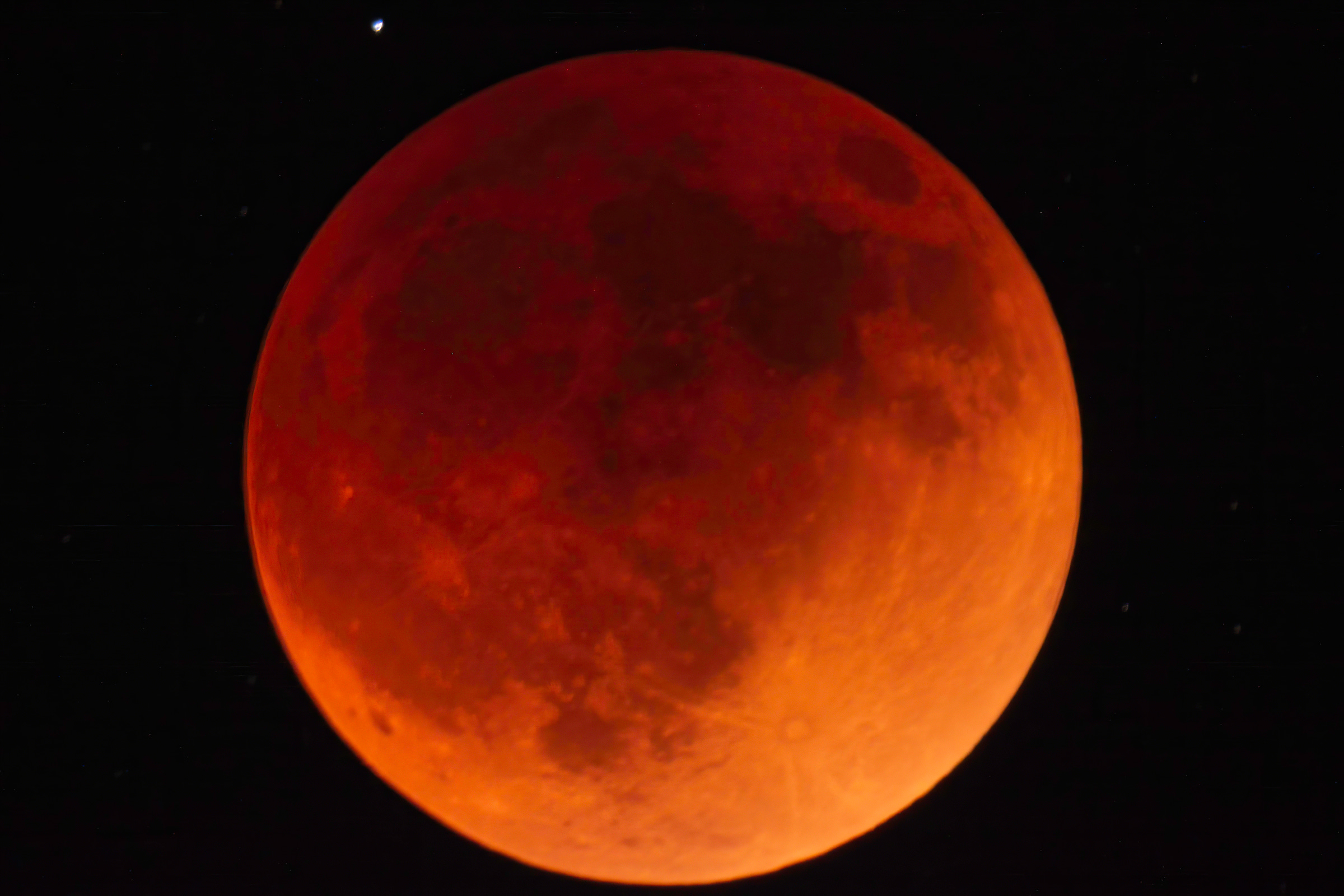 the total lunar eclipse showing the moon and its surface in shades of red against a black sky and a single star above the moon toward the left