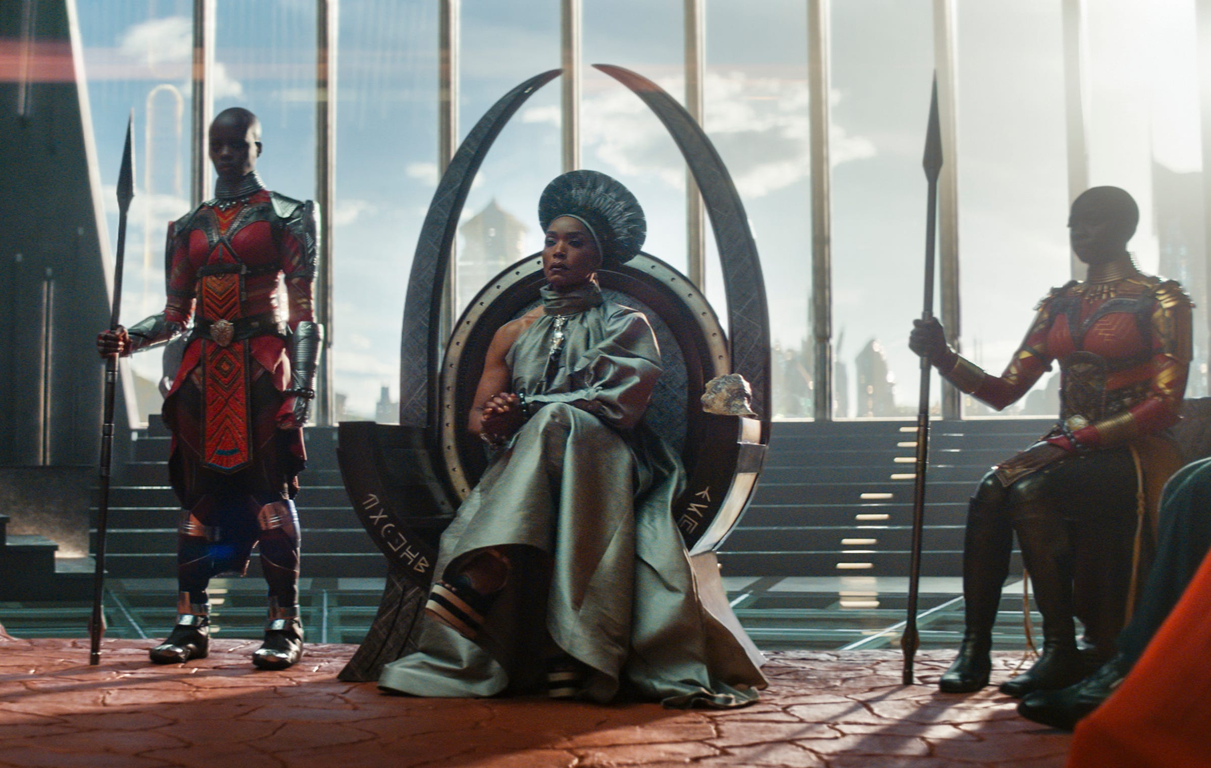 Angela Bassett as Queen Romanda sitting on the throne of Wakanda, flanked by two Dora Milaje